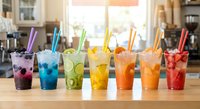 Colorful rainbow drinks with straws lined up on wooden counter in modern kitchen setting for summer beverage menu and refreshment concepts.