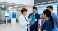 Female doctor explaining lung X-ray to diverse medical team in modern hospital corridor. Healthcare professionals discussing pulmonary diagnosis and treatment.