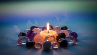 Glowing candle surrounded by colorful glass marbles creates peaceful meditation atmosphere for relaxation and mindfulness practices.