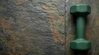 Green dumbbell weight on rustic stone texture background for fitness, gym training, strength exercise, and workout equipment concepts.