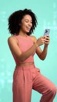 Happy young African American woman in pink outfit using smartphone on turquoise background with bokeh lights for social media and technology concepts.
