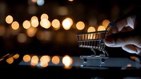 Hand pushing miniature shopping cart on reflective surface with glowing bokeh lights in background, creating modern retail and e-commerce concept.
