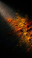 Vibrant orange and red spice powder scattered on dark textured surface with dramatic lighting creating warm glow and artistic shadows for culinary design.