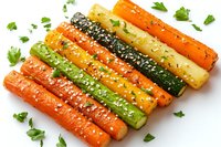 Colorful roasted baby carrots and zucchini garnished with sesame seeds, herbs and spices arranged in parallel rows on white background, healthy vegetarian dish.
