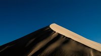 Smooth sand dune ridge with contrasting light and shadow against clear blue sky, suitable for travel, nature, and desert landscape backgrounds.