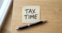 Yellow sticky note with TAX TIME text and black pen on wooden desk surface for financial planning and accounting preparation during filing season.