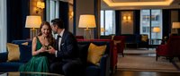 Elegant couple in formal attire sharing intimate moment on luxury hotel lobby sofa with warm ambient lighting and sophisticated interior design.