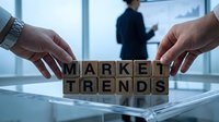 Business professionals arranging wooden blocks spelling market trends on glass table in modern office with colleague presenting in background.