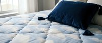 Cozy bedroom scene featuring a neatly made bed with blue and white quilted bedding and a dark navy pillow with tassels, perfect for home decor and lifestyle content.
