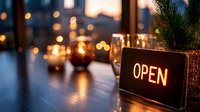 Warm glowing open sign on wooden table with candles and pine branch creating cozy restaurant or cafe atmosphere for holiday business marketing.
