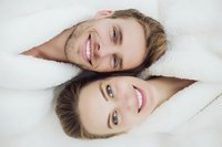 Young Caucasian couple smiling in white bathrobes, faces close together in intimate portrait showing happiness and connection.