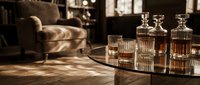 Whiskey decanters and glasses arranged on a table in a luxurious living room with warm lighting and comfortable seating in the background.