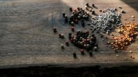 Mixed peppercorns and spices scattered on rustic wooden surface with warm lighting for culinary cooking and seasoning applications.
