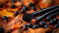 Professional makeup brushes with black bristles on autumn maple leaves background with scattered black decorative beads creating seasonal beauty composition.
