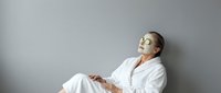 Relaxed middle-aged Caucasian woman in white bathrobe sitting peacefully with eyes closed against gray wall, spa wellness meditation concept.