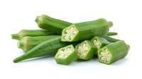 Fresh green okra pods whole and sliced showing star-shaped cross sections isolated on white background for healthy cooking and recipe designs.