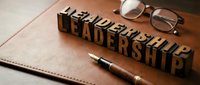 Wooden letterpress blocks spelling leadership on a leather notebook with a fountain pen and glasses, symbolizing business success and management.