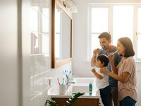 Happy Asian family with young child brushing teeth together in modern bathroom during morning routine creating healthy habits and bonding moments.