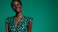 Young African woman with bright smile wearing leopard print dress on emerald green background, fashion portrait in studio lighting.
