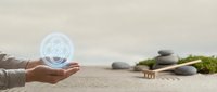 Hand holding glowing holographic mandala symbol above zen garden with stacked stones and moss for meditation and spiritual wellness practices.