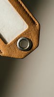 Close-up detail of brown leather luggage tag corner with metal grommet eyelet showing craftsmanship and texture for travel accessories branding.