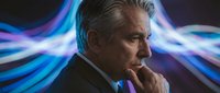 Mature man in business suit contemplating with glowing blue light trails in background, representing innovation, technology, and strategic thinking for corporate concepts.