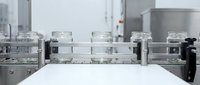 Empty glass jars moving on automated conveyor belt in modern pharmaceutical or food processing facility for industrial packaging applications.