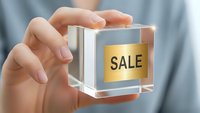 Hand holding transparent glass cube with golden sale label for retail marketing and promotional campaigns in business commerce.