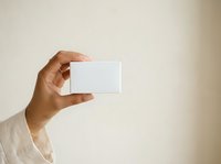 Male hand with medium skin tone holding blank white business card against neutral beige background for branding and corporate identity mockups.