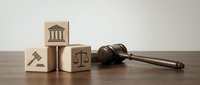 Wooden gavel and blocks with legal symbols including courthouse, scales of justice and hammer on desk representing law, justice system and legal services.