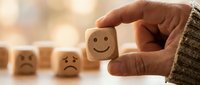 Hand selecting wooden cube with happy face emoji from row of sad faces representing positive choice and optimism in decision making.