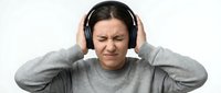 Young woman covering ears with hands showing discomfort from loud noise or headache, wearing gray sweater on white background isolated for design use.