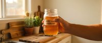 Hand holding mason jar of golden kombucha tea in sunlit kitchen with fermented probiotic drink for healthy lifestyle and wellness nutrition.