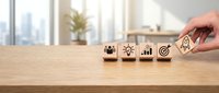Hand placing wooden cubes with business strategy icons on office desk. Corporate planning and goal setting concept for presentations and marketing.