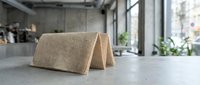 Folded beige linen napkin on concrete countertop in modern kitchen with industrial windows and potted plants, suitable for hospitality and home decor design.