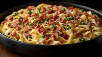 Creamy pasta dish with crispy bacon bits, green peas, and parmesan cheese in rich sauce, served in black pan against dark background. Close up food photography.