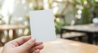Hand holding blank white card mockup with blurred outdoor cafe background for business presentation and marketing materials.