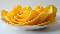 Fresh ripe mango slices arranged in curved shapes on white ceramic plate, bright yellow tropical fruit with soft natural lighting for food photography.