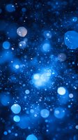 Magical blue bokeh lights and glowing particles floating in dark space create dreamy atmospheric background for festive designs and holiday projects.