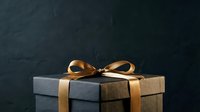 Wrapped gift box with gold ribbon bow on dark slate background, suitable for holiday, celebration, and luxury retail marketing materials.