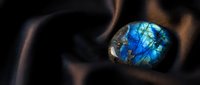 Stunning labradorite gemstone with brilliant blue flash resting on smooth dark fabric surface showcasing natural iridescent colors and mystical properties.