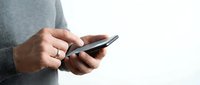 Person using smartphone with both hands typing or browsing on mobile device screen against neutral background for communication and technology concepts.