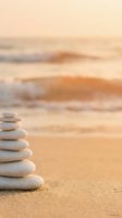 Zen stone stack on sandy beach at sunset with soft ocean waves creating peaceful meditation and mindfulness atmosphere for wellness and relaxation concepts.