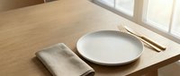 Empty white plate with gold fork and knife on wooden table with beige napkin, minimalist dining setup for restaurant, catering, or food service design projects.