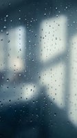 Raindrops covering window glass with blurred cityscape background, conveying rainy weather atmosphere suitable for weather-related designs and seasonal content.