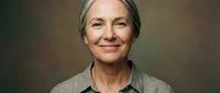 Mature woman with gray hair and fair complexion wearing casual gray shirt against neutral background, suitable for healthcare, wellness, lifestyle and corporate applications.