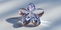 Crystal clear glass flower ornament with prismatic reflections casting rainbow shadows on white surface for luxury decor and jewelry design projects.