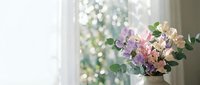 Fresh spring flower bouquet with purple and pink blooms in white vase by bright window creating soft natural lighting for home decor and interior design.