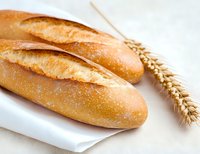Fresh crusty baguettes with golden brown crust on white linen napkin alongside wheat ear, showcasing traditional French bread baking and bakery products.