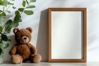 Brown teddy bear next to wooden frame mockup on white wall with green plant shadow, modern minimal home decor composition for nursery or kids room.